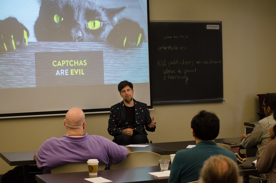 Nic Steenhout talking to class attendees in front of a slide with a cat. The caption reads "CAPTCHAs are evil"