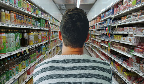 Man viewed from the back in the middle of a grocery store aisle